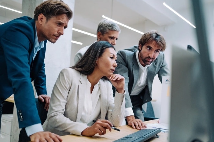 Small team collaborating around a computer reviewing business information in a modern office